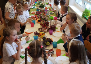 Dzieci siedzą przy wspólnym stole przy słodkim poczęstunku